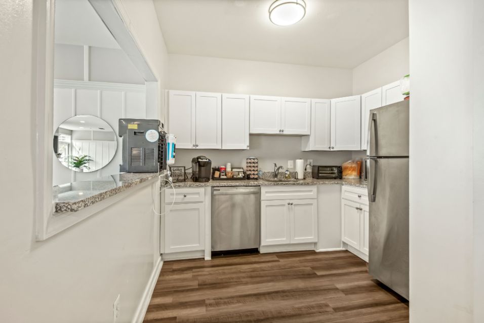 A Kitchen with white walls, white cabinets, tan counters, medium-brown hardwood floor, and stainless-steel dishwasher and refrigerator